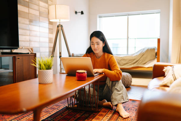 Young woman using laptop comfortably at home A young woman is using a laptop comfortably in the living room at home. japanese woman stock pictures, royalty-free photos & images