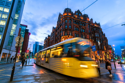 Manchester City centre, City tram approaching with pedestrians walking on the road.