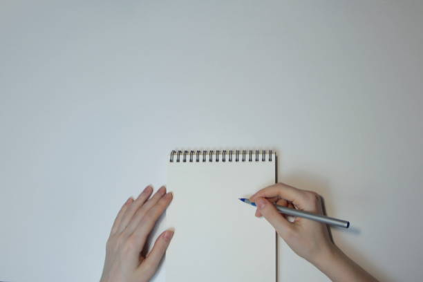 istock Hands with a ballpoint pen and with a blank notebook on a white table 1202760609