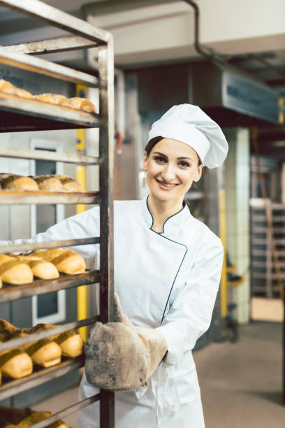 istock Baker woman pushing sheets with bread in the baking oven 1202764099