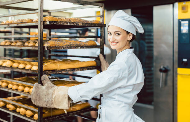 Baker woman pushing sheets with bread in the baking oven Baker woman pushing sheets with bread in the baking oven wearing bakers mittens baker occupation stock pictures, royalty-free photos & images