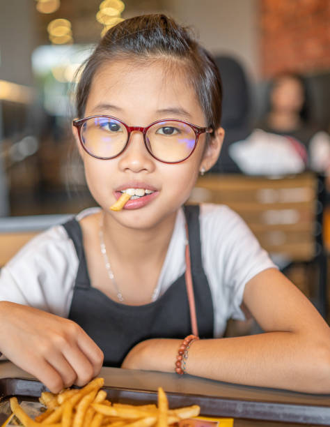 Medium shot of a young girl eating french fries Medium shot of a young girl sitting at restaurant eating french fries. girls getting ready to go out stock pictures, royalty-free photos & images
