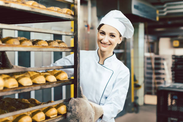 istock Baker woman pushing sheets with bread in the baking oven 1202764383