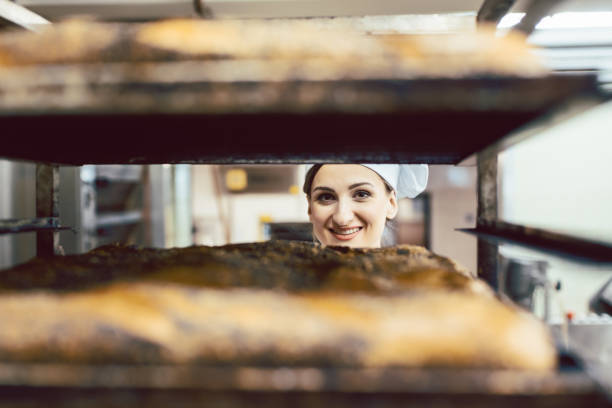 istock Beautiful baker woman looking though bread on sheets 1202764395