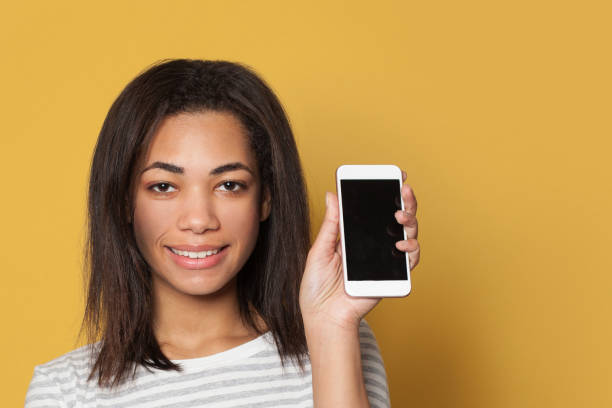 istock Young attractive woman showing empty cell phone display on yellow background 1202767396