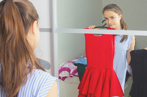 The girl at home in front of the mirror tries on dresses, chooses an outfit