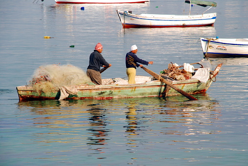 Fish nets and prawn traps stacked on stern deck of fishing vessel moored at Fishermans wharf, with a tow boat bow and mooring lines