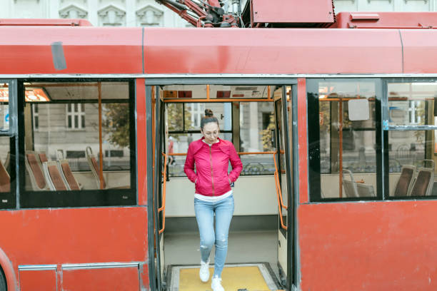 Young positive Asian hipster woman passenger getting off the yellow bus in vacation. Lifestyle and everyday routine concept.