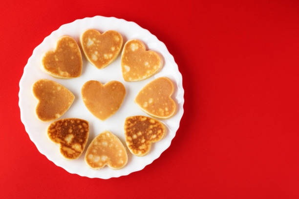 Creative breakfast for Valentine's Day. Heart shaped pancakes on a white plate, on a red background. Valentine's day background. Top view. Flat lay. Copy space