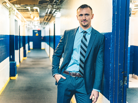 Young fit man in business suit after the hockey training in hallway of changing room.