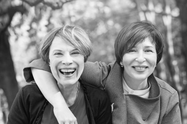 laughing women hugging and having fun in park, tonned black and white retro portrait - couple walking old middle imagens e fotografias de stock