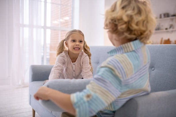 istock Two blond kids playing with pillows on the sofa and looking angry 1202783809
