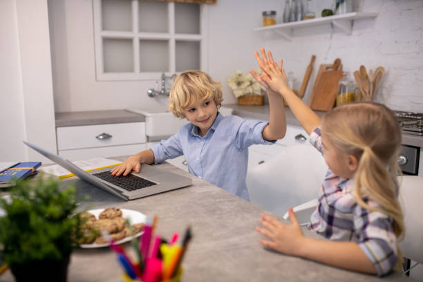 istock Two kids sitting at the table and making high five 1202784093