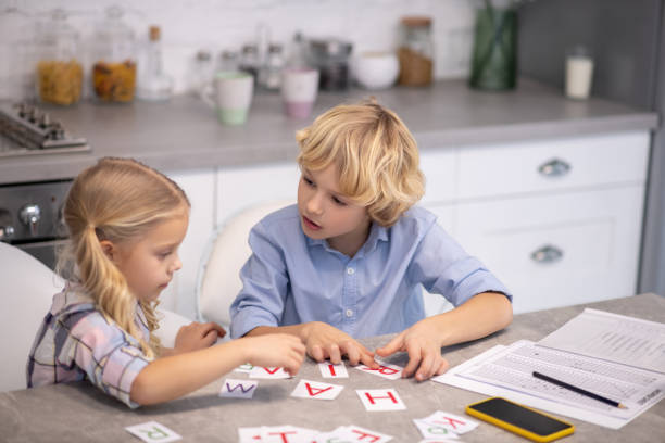 istock Two blond kids putting cards with letters on the table and looking involved 1202784224