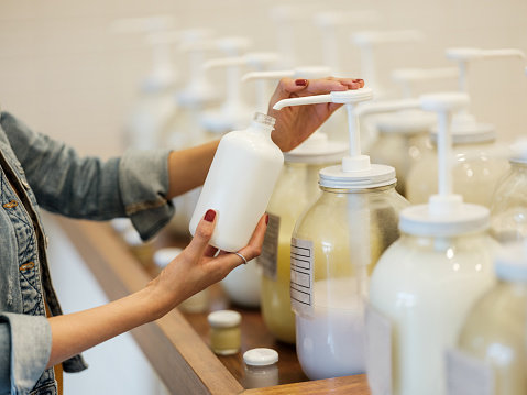 A young latin woman holding and filling up glass container with lotion at the zero waste store.
