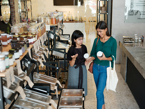 A young latin woman standing next to the seller and asking her information about products in the zero waste store.