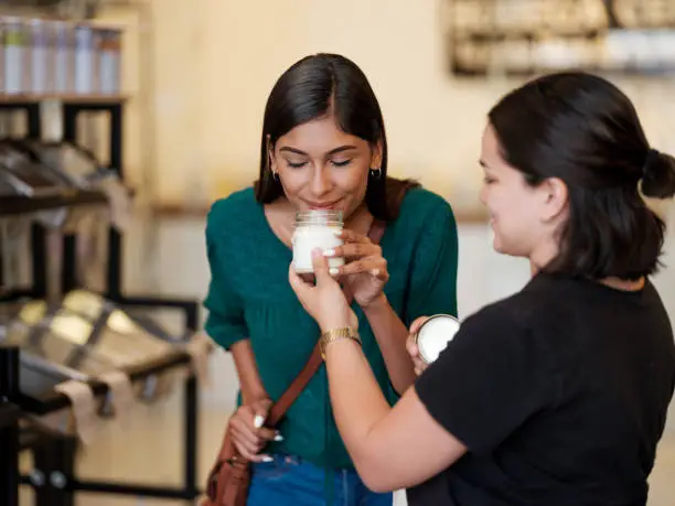 A lovely female costumer smelling a product from a glass container held by the young seller.