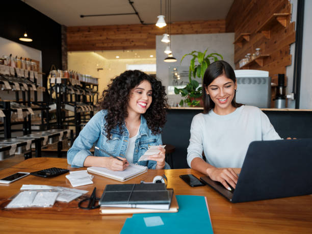 Happy young women sitting at table in store and using laptop