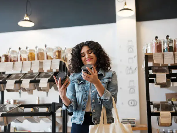 A happy latin female costumer holding jars in an eco-friendly store and smiling.