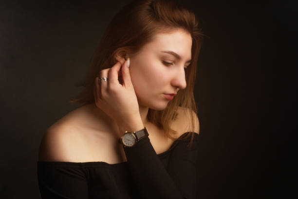 portrait in the photo studio of a brown-haired girl, on a black background in black clothes with open shoulders. short hair. - earring human face brown hair black hair imagens e fotografias de stock