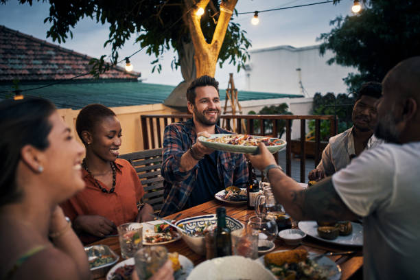 We're real friends if we share food Shot of a group of young friends having a dinner party outdoors south african braai stock pictures, royalty-free photos & images