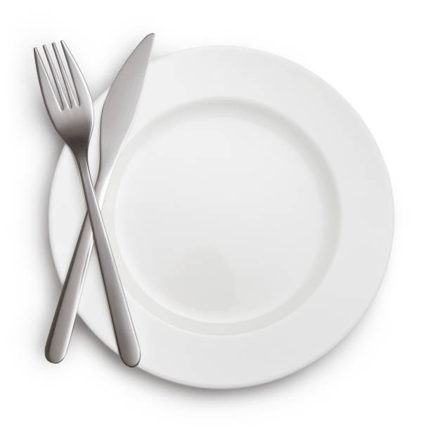 istock Fork and knife crossed on white plate on white 1202792866