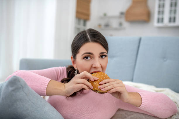 Full-figured young woman in a pink shirt eating a burger Burger. Full-figured young woman in a pink shirt eating a burger brat burger stock pictures, royalty-free photos & images