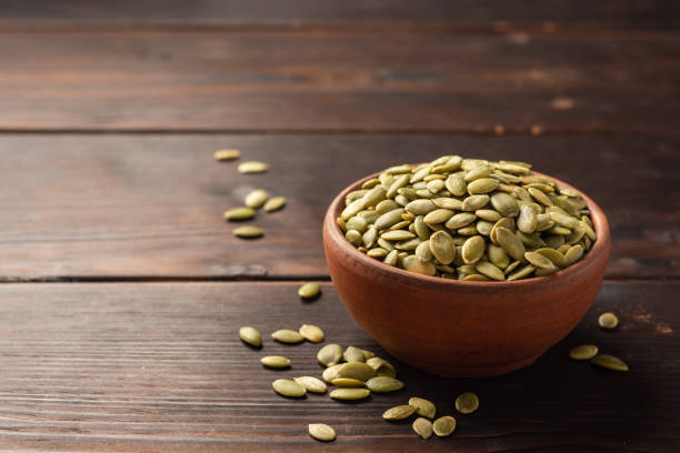 istock Pumpkin seeds in ceramic bowl on dark wooden background 1202794067