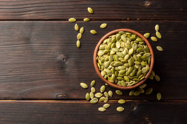 istock Pumpkin seeds in ceramic bowl on dark wooden background 1202794074