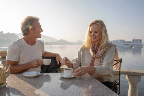 Mature couple enjoy tea with lake and floating palace behind Lake Pichola, Udaipur lake palace stock pictures, royalty-free photos & images