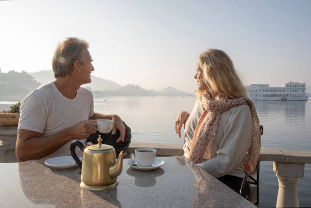 Mature couple enjoy tea with lake and floating palace behind Lake Pichola, Udaipur lake palace stock pictures, royalty-free photos & images