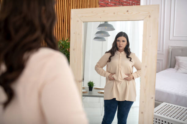 mujer joven con una blusa beige tocando su vientre - overweight women weight loss fotografías e imágenes de stock