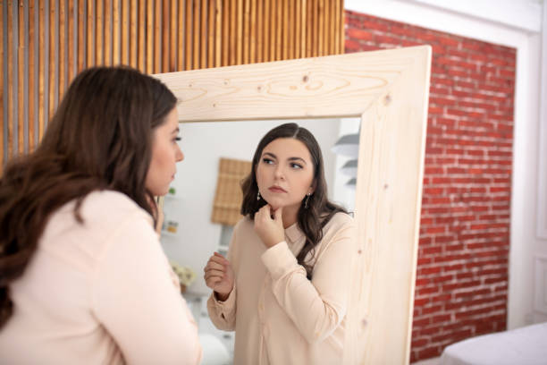 istock Young woman in a beige blouse examining her face 1202795561