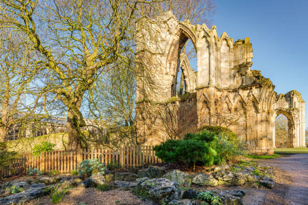People enjoying a sunny October afternoon in the Museum Gardens in central York, England. The ruins of St Mary's Abbey (1294, Simon of Pabenham) are in the background. The ruins are a Scheduled Monument.
