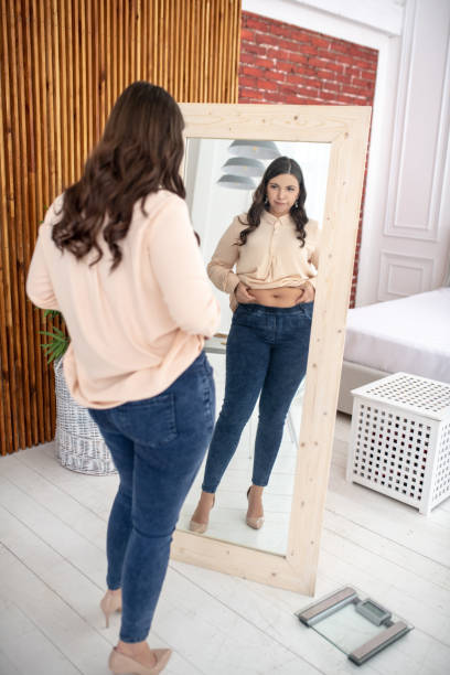 istock Young woman in a beige blouse looking at herself 1202795594