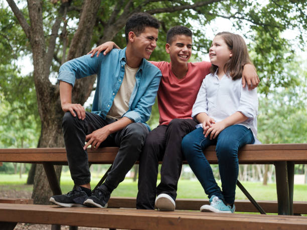istock Playful mexican siblings sitting on bench at park and laughing 1202800627