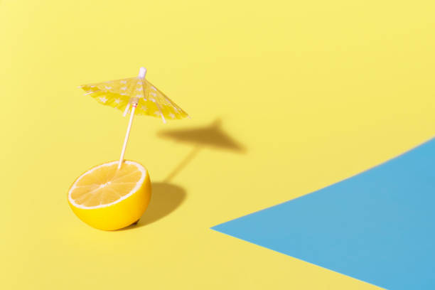 citron avec un parapluie de cocktail dans la lumière du soleil. contexte de chaleur d'été - drink umbrella umbrella drink isolated photos et images de collection