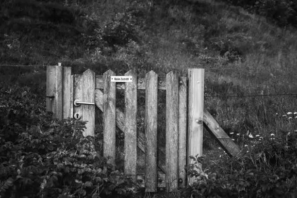 Weathered wooden gate with no entrance message in german, surrounded by rose bushes, on Sylt island, Germany. Old garden door in black and white