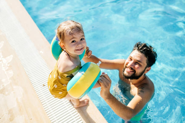 linda niña divirtiéndose con los padres en la piscina - floatation device fotografías e imágenes de stock