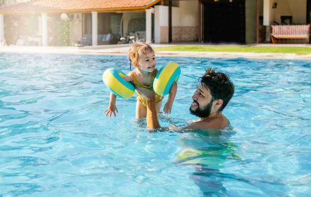 istock Cute little girl having fun with parents in pool 1202814886