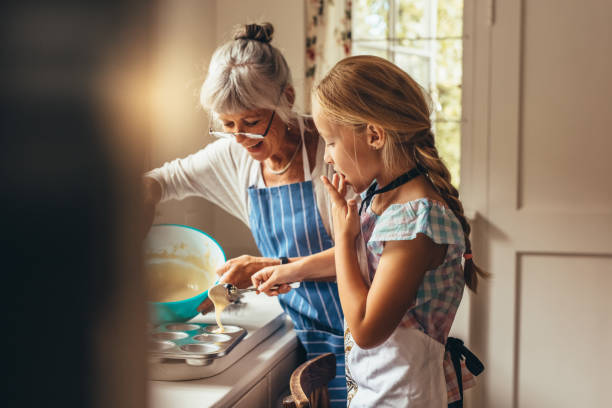 Granny and kid making cup cakes Grandmother teaching kid to make cup cakes. Happy grandmother and kid pouring cake batter in cup cake moulds. grandmother stock pictures, royalty-free photos & images