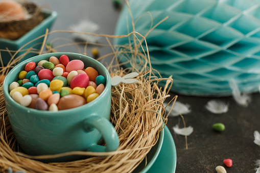 Colorful candies, and Easter eggs in a blue cup on the table as a part of a creative Easter table decoration.