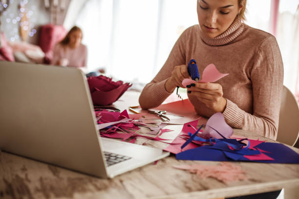 istock Creative young woman using hot glue gun while making decorative paper flowers 1202845516
