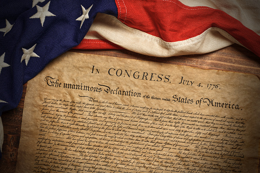 A copy of the United States Declaration of Independence with a vintage American flag on a wood background