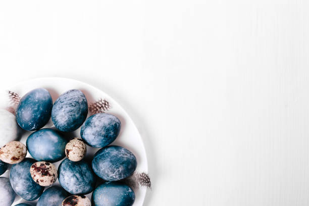 istock Beautiful group ombre blue Easter eggs with quail eggs and feathers on a white wooden background. Easter concept. Border eggs. Copy space for text. 1202845836