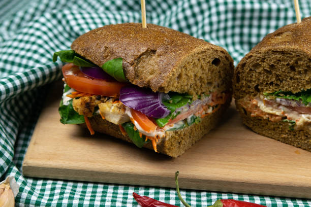 istock A dark bread sandwich ut in half with chicken, tomatoes, spinach, cheese and carrots stands on a wooden board 1202846760
