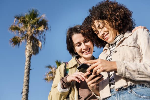 two young women watching the phone multiracial couple of young women looking at a cell phone while smiling, concept of technology and racial diversity free girl download stock pictures, royalty-free photos & images