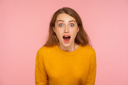 Wow, amazing! Portrait of excited surprised ginger girl in sweater looking at camera with astonishment, shocked by unexpected success, crazy news. indoor studio shot isolated on pink background