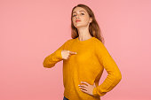 This is me! Portrait of attractive haughty ginger girl in sweater pointing at herself and looking at camera with arrogance