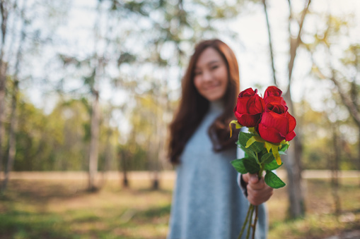 Closeup image of a beautiful asian woman holding and giving red roses flower on Valentine's day